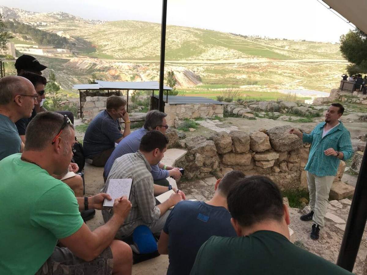 Cliff Johnson teaching a group of men taking notes among ancient stone ruins on a hillside in Israel